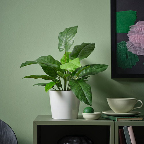 Pequeña planta verde FEJKA en maceta se encuentra en el estante junto a la taza y el tazón, iluminando la habitación con hojas vibrantes y realistas.