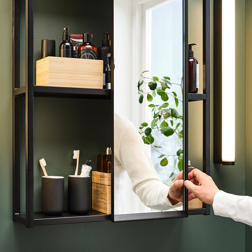 Persona ajustando el espejo corredizo junto a la estantería del baño con artículos de tocador.