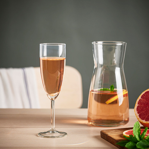Copa de champán junto a jarra con rodajas de pomelo sobre mesa de madera.