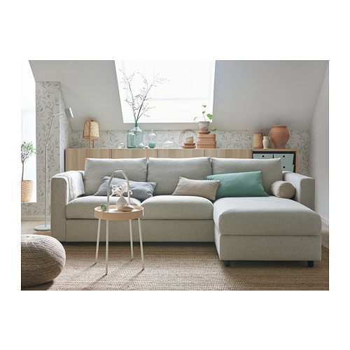 Sala de estar moderna con sofá seccional VIMLE gris claro, almohadas verde azulado, mesa auxiliar de madera y decoración de pared verde.