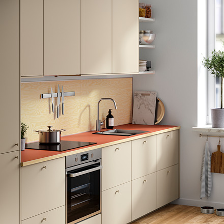 Cocina moderna con gabinetes cremosos, encimera de color óxido, electrodomésticos de acero inoxidable, placa para salpicaduras de madera y vegetación colgante.