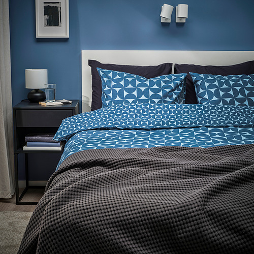 Dormitorio azul con edredón ÄNGSNEJLIKA, paredes oscuras, elegante mesita de noche.