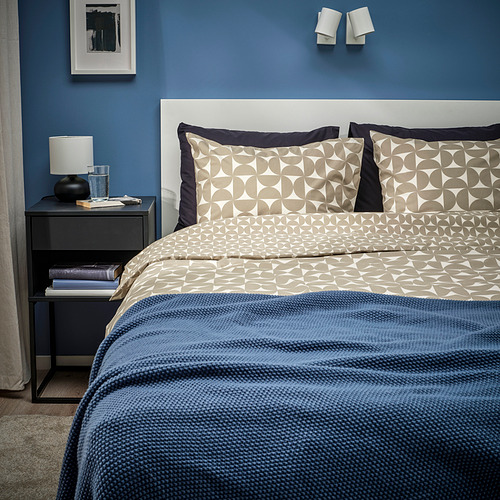 Dormitorio moderno con ropa de cama ÄNGSNEJLIKA, pared azul, manta y cabecero de madera.
