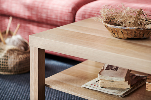 Una mesa de centro de madera clara con un sofá rojo y una cesta decorativa detrás.