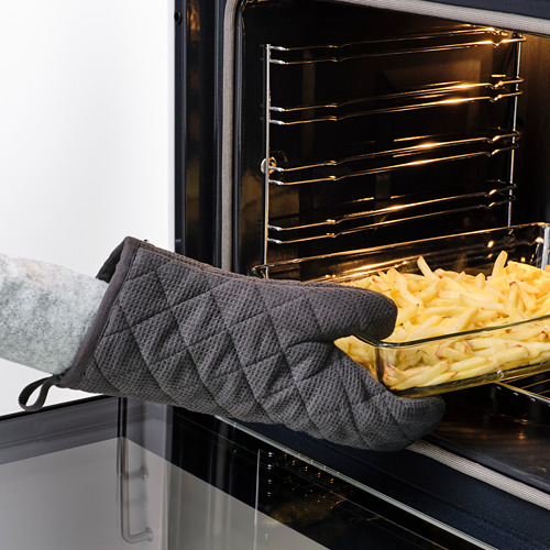 Persona con guantes grises RINNIG colocando una bandeja de comida en el horno. Los guantes protegen las manos del calor.