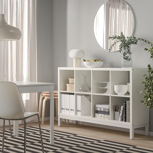 Estanterías blancas KALLAX con libros, cuencos, jarrones y una lámpara en una habitación minimalista.