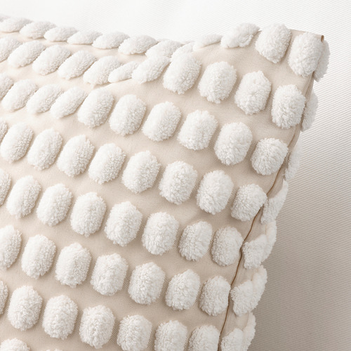 Funda de cojín texturizada con innumerables puntos blancos esponjosos sobre un fondo beige, creando una sensación suave y acogedora.