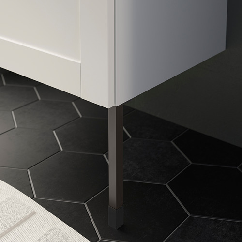 Mueble de baño blanco sobre pavimento hexagonal negro, sostenido por patas negras regulables.