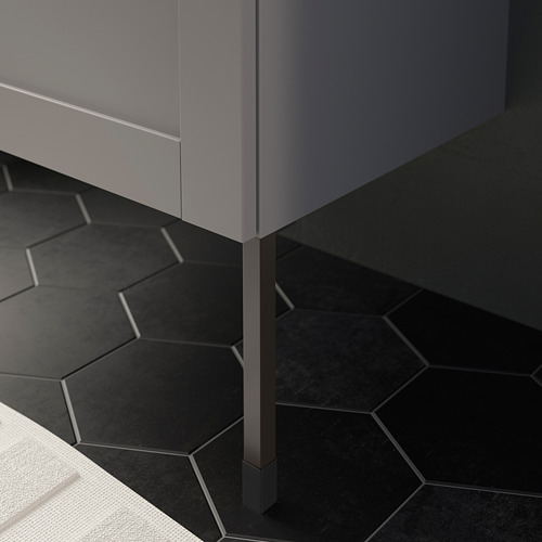 Moderno mueble de baño gris sobre patas metálicas, colocado sobre azulejos hexagonales negros.