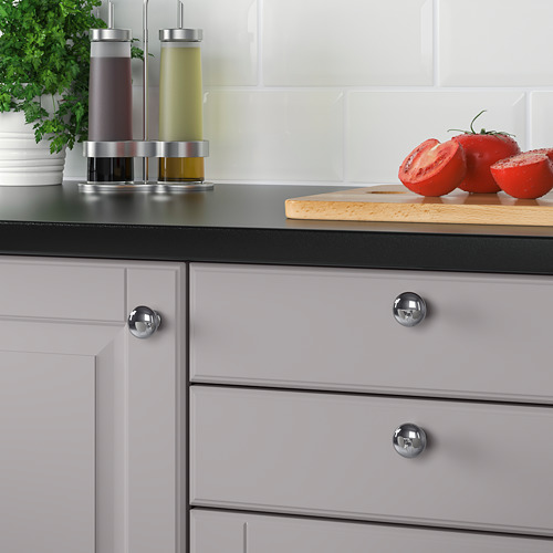 Muebles de cocina modernos con pomos redondos cromados. Los tomates se colocan en una tabla de cortar de madera junto a las hierbas.