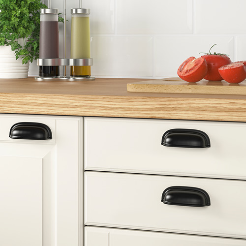 Encimera de cocina de madera con asas de tazas negras, utilizada para sujetar condimentos y cortar tomates.