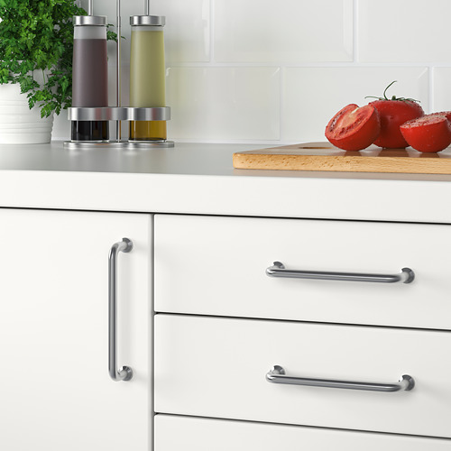 Cocina moderna con gabinetes blancos y manijas de acero inoxidable. Encimera una tabla de cortar con tomates en rodajas y dispensadores de condimentos.