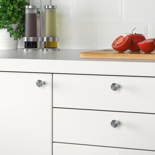 Cocina moderna con armarios blancos con pomos de acero inoxidable BAGGANÄS. La encimera tiene tomates y condimentos.