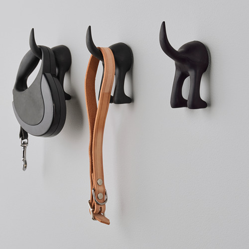 Tres ganchos decorativos negros con cabeza de perro en una pared, uno con una correa negra y otro con un cinturón de cuero marrón.