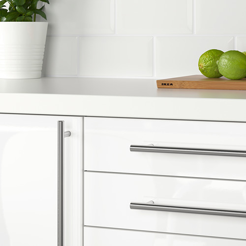 Cocina moderna con armarios blancos y tiradores metálicos. Una encimera blanca sostiene una planta y limas.