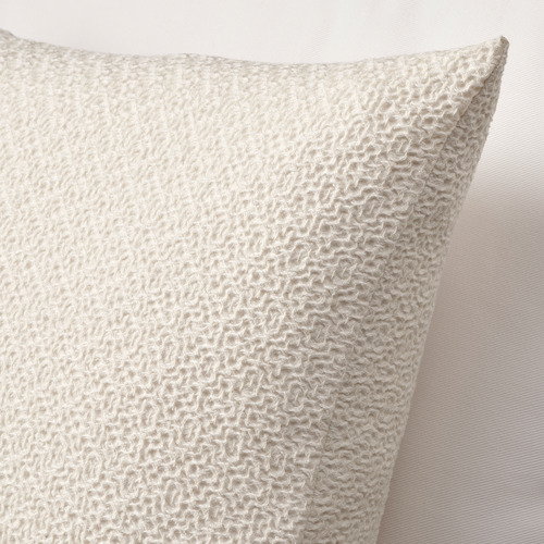 Cojín beige con textura de punto, suave tacto de algodón, cierre de cremallera visible.