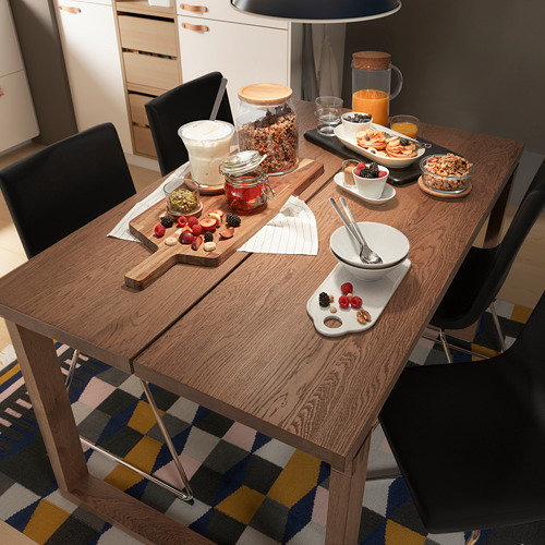 Cocina moderna con mesa de roble y sillas negras, artículos de desayuno en mesa de madera.