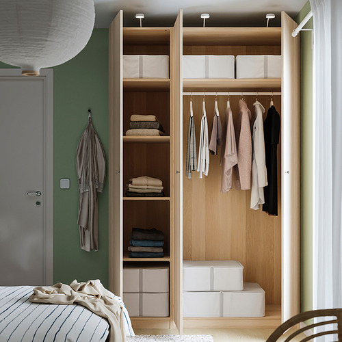 Armario de madera con puerta abierta, ropa en perchas y artículos doblados en estanterías, junto a la cama.