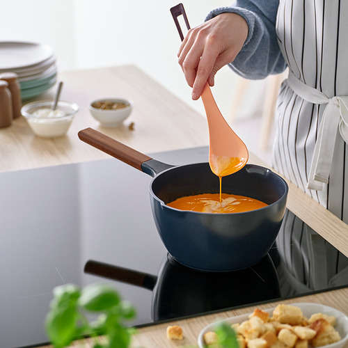 Una persona revuelve la sopa de naranja en una sartén azul con una cuchara de colores con mango de madera. El diseño estrecho de las cucharas ayuda a la precisión.