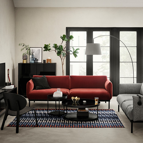 Sala de estar moderna con sofá rojo en forma de L, sillón gris, mesas auxiliares redondas de vidrio negro, alfombra colorida y grandes ventanales que permiten la entrada de luz natural.