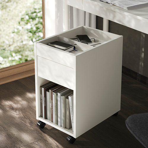 Pequeña unidad de almacenamiento móvil blanca con cajón, que sostiene libros debajo y artículos tecnológicos en la parte superior, ideal para organizar el espacio de oficina.