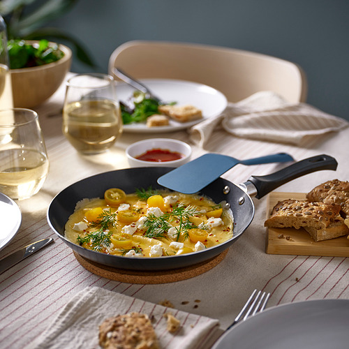 Configuración del desayuno con sartén gris, plato amarillo, platos, pan, vasos y ensaladera.