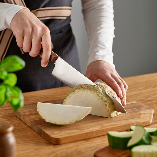 Persona cortando verduras en una tabla de cortar de madera con un cuchillo afilado y bien equilibrado.