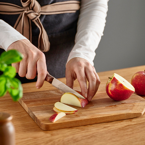 La persona corta la manzana en rodajas en una tabla de cortar de madera con un cuchillo VARDAGEN.