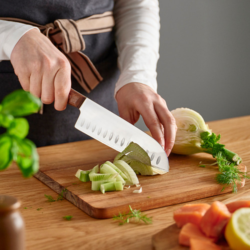 Una persona está cortando verduras en una tabla de cortar de madera con un cuchillo santoku con hendiduras.