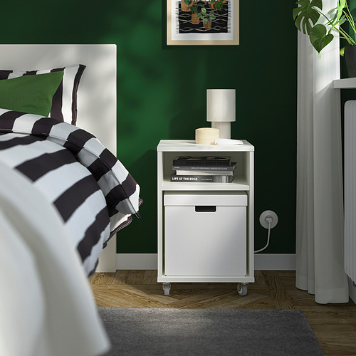 Dormitorio moderno con paredes verdes, mesita de noche blanca al lado de la cama, lámpara, libros y planta, que exhibe una caja FJÄDERHARV para almacenamiento.