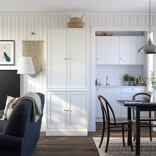 Sala de estar moderna con mueble de madera blanca HAVSTA contra la pared a rayas. Sillón azul, juego de comedor de madera y decoración elegante.