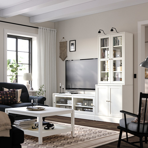 Sala de estar moderna con muebles HAVSTA, banco de vidrio para televisión, cortina negra, sofá oscuro, alfombra estampada, piso de madera.