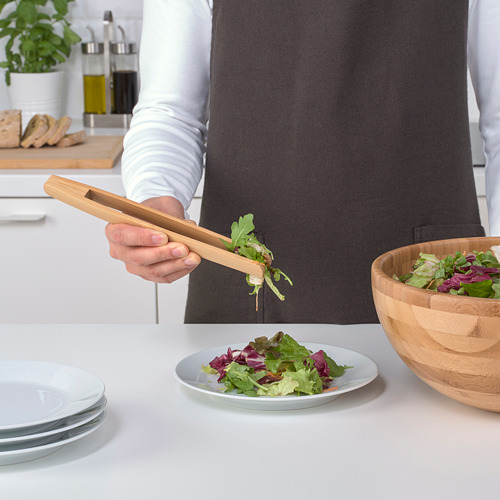 Persona que usa pinzas de bambú para servir ensalada de un tazón en un plato. Las pinzas seleccionan efectivamente ingredientes específicos para ensaladas.