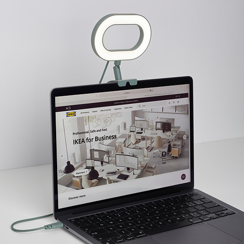 Ordenador portátil con lámpara de anillo adjunta, que muestra el sitio web de ikea. La lámpara ilumina al usuario para reuniones de video, intensidad de luz ajustable y temperatura de color.