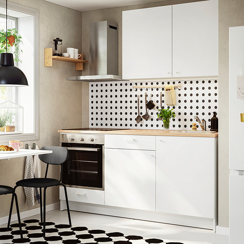 Moderna configuración de cocina blanca. Salpicadero de lunares negros, estante de madera, horno pequeño, accesorios de mostrador. El diseño compacto se adapta bien a las cocinas más pequeñas.