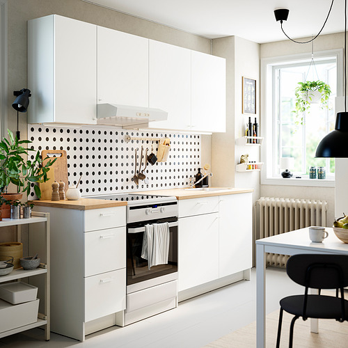 Cocina blanca moderna con placa para salpicaduras de lunares negros, electrodomésticos de acero inoxidable, plantas colgantes y sillas negras.