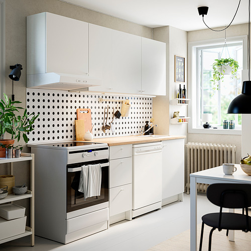 Pequeña cocina blanca con gabinetes KNOXHULT, placa para salpicaduras de lunares, horno de acero inoxidable, encimera de madera, diseño eficiente, estantes de pared y área de comedor.