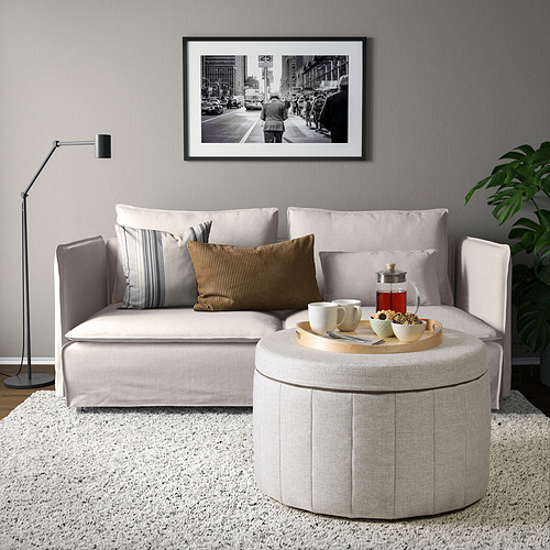 Sala de estar moderna con sofá en forma de L, otomana, lámpara, foto de la calle y planta.