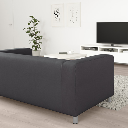 Sala de estar moderna con sofá KLIPPAN negro, mesa de centro blanca, tv en soporte, planta y arte abstracto en la pared.