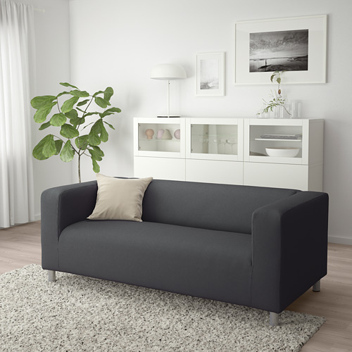 Sala de estar moderna con sofá KLIPPAN gris, gabinete blanco, planta verde y alfombra.