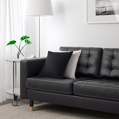 Sala de estar moderna con sofá de cuero negro, dos almohadas y una mesa auxiliar con una planta.