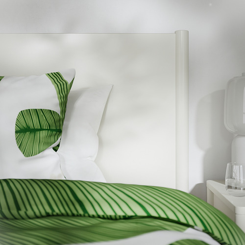 Cama blanca minimalista con ropa de cama verde estampada de hojas, cajones de cierre suave.
