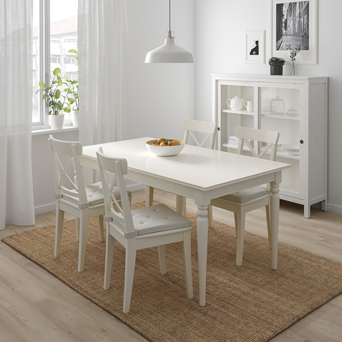 Juego de comedor blanco con sillas, alfombra, lámpara colgante y aparador de estilo minimalista.