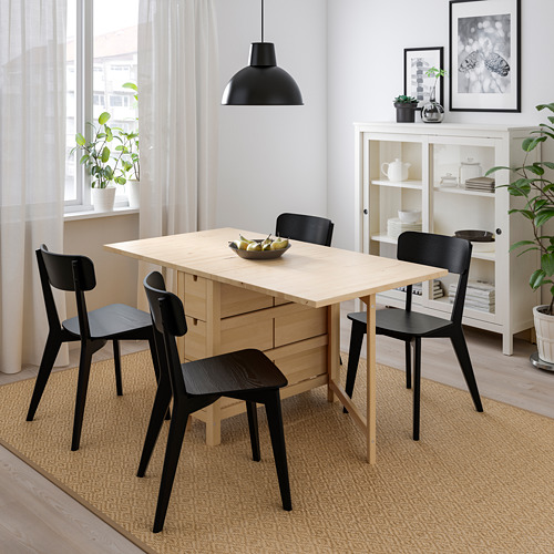 Pequeña mesa de comedor plegable de madera clara y cuatro sillas oscuras en una habitación acogedora.