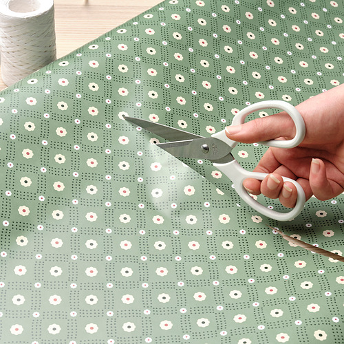 Persona cortando papel de regalo floral con tijeras.