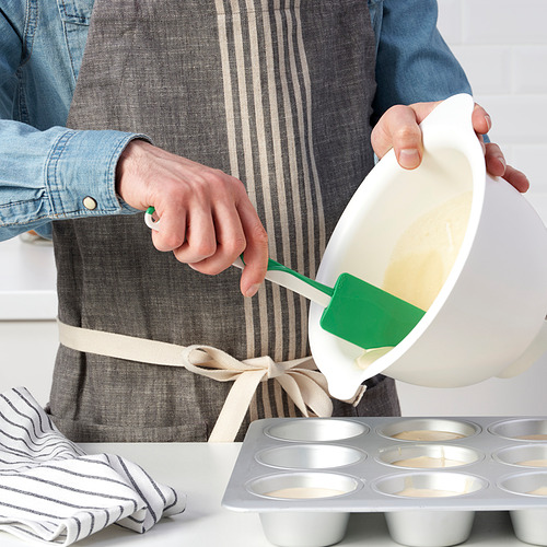 La persona vierte la masa en un molde para muffins con una espátula verde.