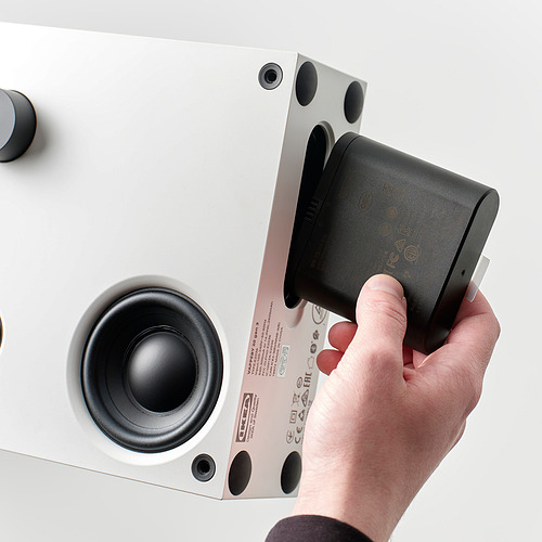 Una persona conecta un dispositivo negro a la parte posterior de un altavoz bluetooth VAPPEBY blanco.