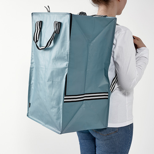Persona que lleva una gran bolsa azul GÖRSNYGG, que contiene mucho y se mantiene en posición vertical. Ideal para diversos artículos y transporte.