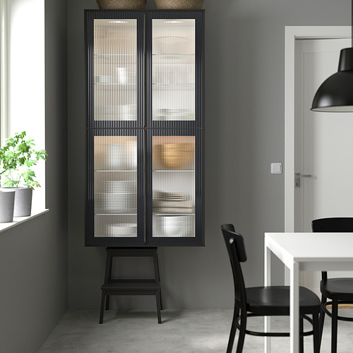 Cocina moderna con mueble alto de cristal HEJSTA negro, más alto que las sillas adyacentes, que muestra elementos decorativos, con un diseño elegante y minimalista.