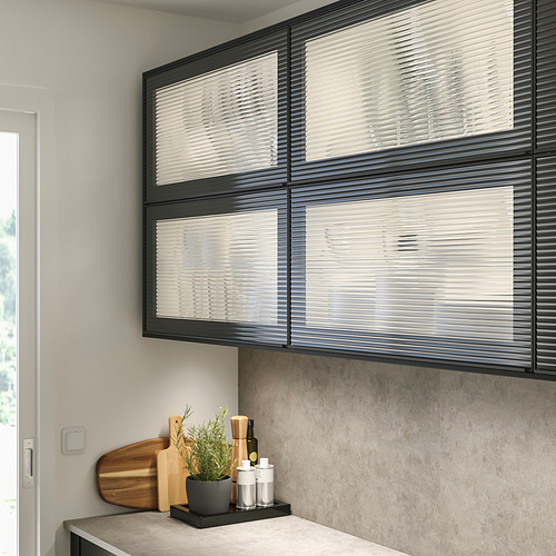 Cocina moderna con vitrinas de cristal negro HEJSTA. Puertas grandes y elegantes con vidrio de caña, colocadas sobre la encimera con artículos pequeños.